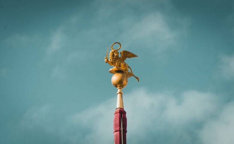 Golden winged lion statue atop a red column against a cloudy sky